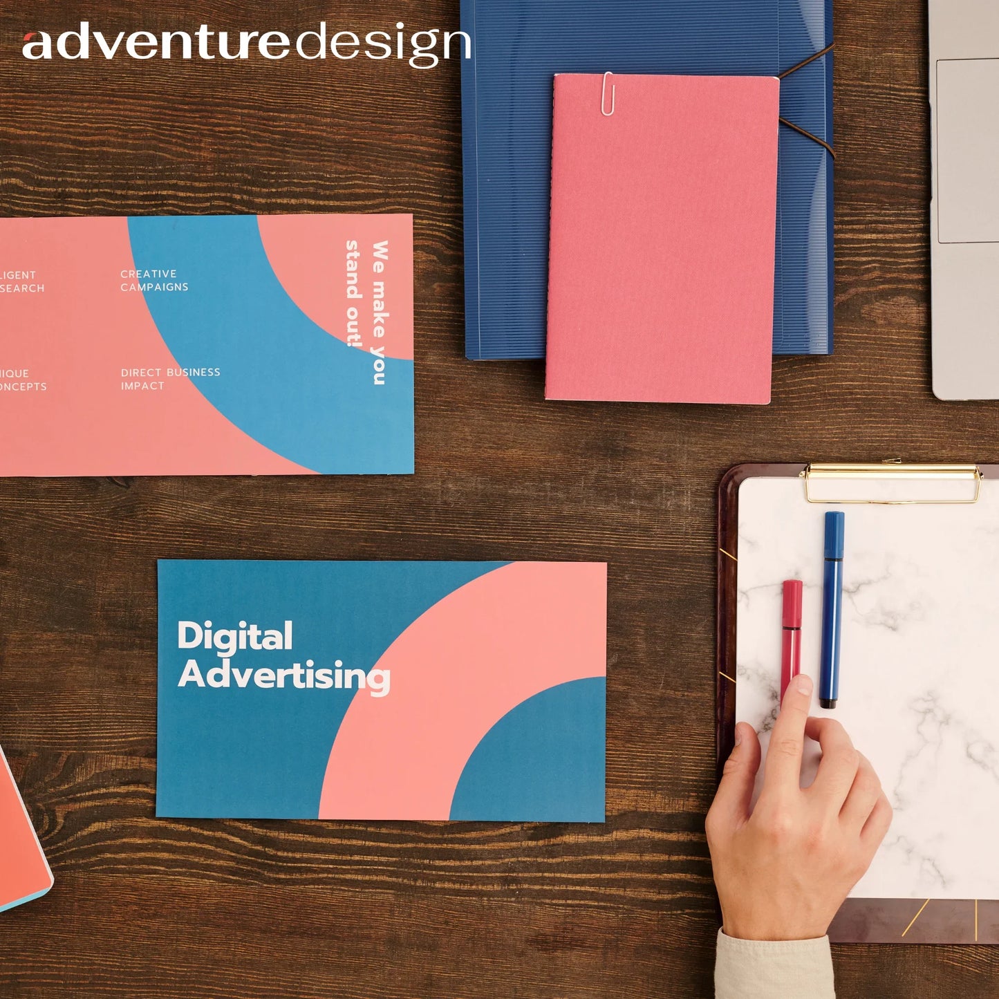 Bureau met Adventure Design flyers voor digitale reclame, notitieboek en hand met stift op houten tafel
