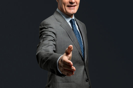 Zakelijke man in grijs pak met blauwe stropdas die hand uitsteekt voor een handdruk, donkere achtergrond