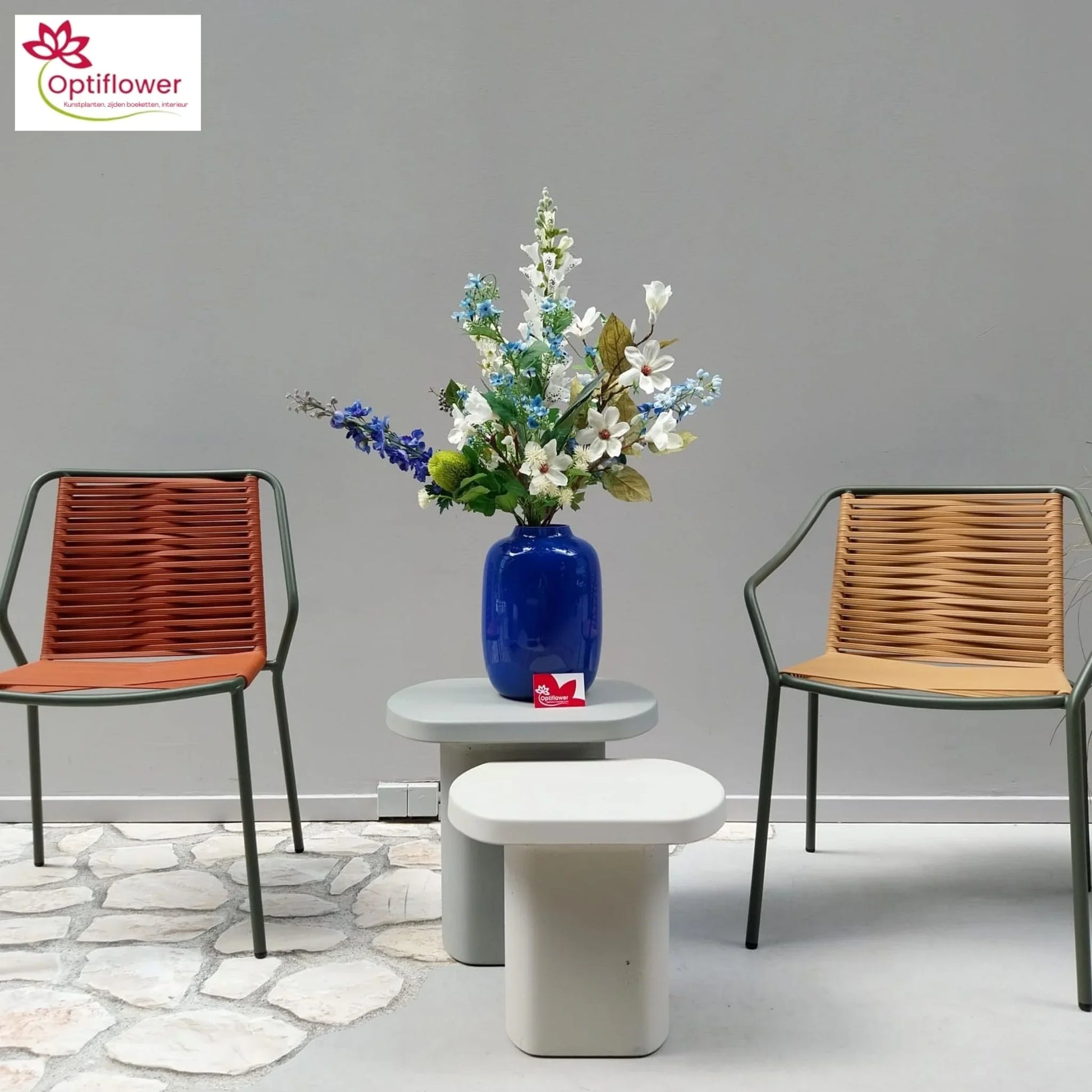 Moderne woonruimte met blauw vaasje en kunstbloemen op grijze tafel, omringd door twee gevlochten stoelen