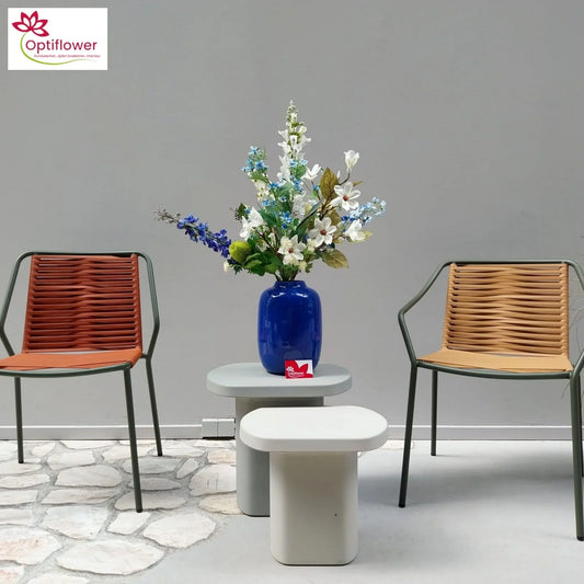 Moderne woonruimte met blauw vaasje en kunstbloemen op grijze tafel, omringd door twee gevlochten stoelen
